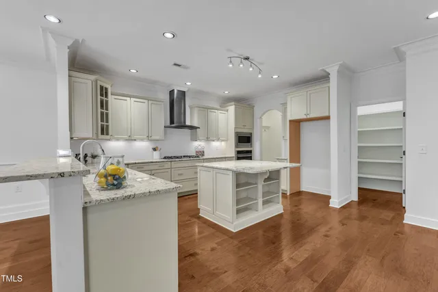 a view of an empty room and a kitchen with wooden floor and a sink