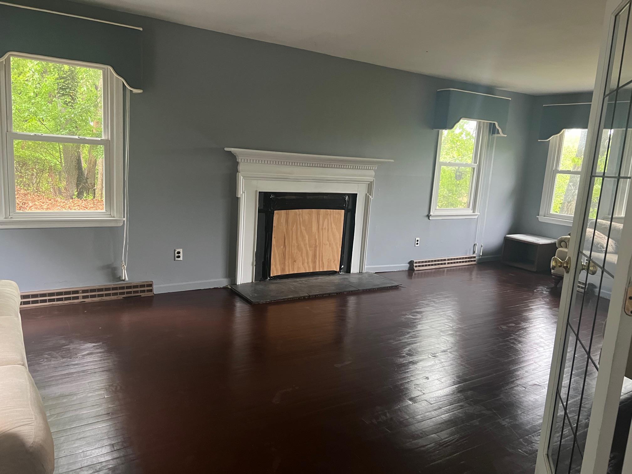 15 Old Field Road Setauket, NY 11733 - Photo 5 of 12 Unfurnished living room featuring baseboard heating, hardwood / wood-style floors, a fireplace with raised hearth, and baseboards