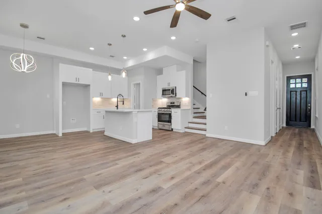 an empty room with wooden floor and kitchen view