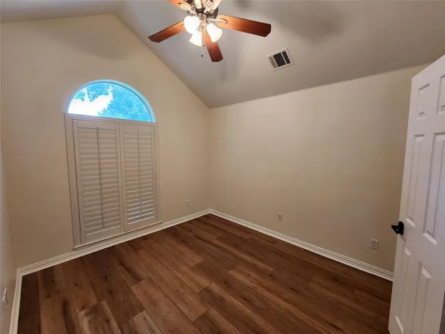 an empty room with wooden floor fan and windows