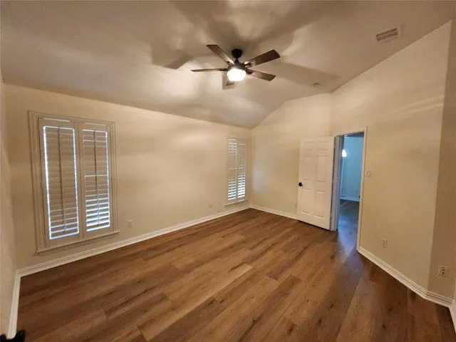 an empty room with wooden floor fan and windows