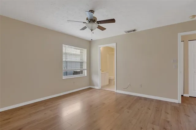 an empty room with wooden floor ceiling fan and windows