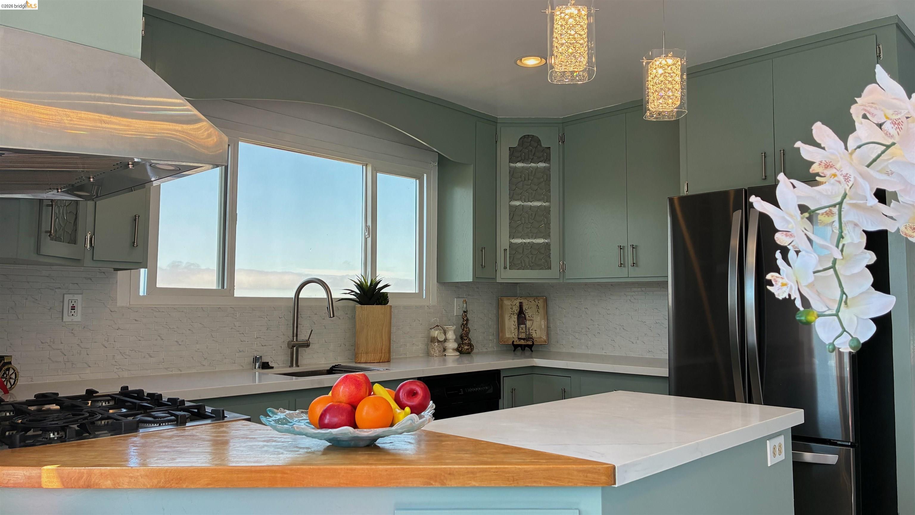 135 Alta Road Oakland, CA 94618 - Photo 9 of 42 Kitchen with range hood, stainless steel appliances, backsplash, glass insert cabinets, and hanging light fixtures
