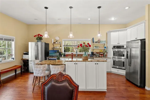 a kitchen with stainless steel appliances kitchen island granite countertop a refrigerator a oven a sink and white cabinets with wooden floor