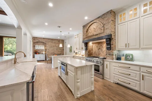 a open kitchen with stainless steel appliances granite countertop a stove top oven a sink dishwasher and white cabinets with wooden floor