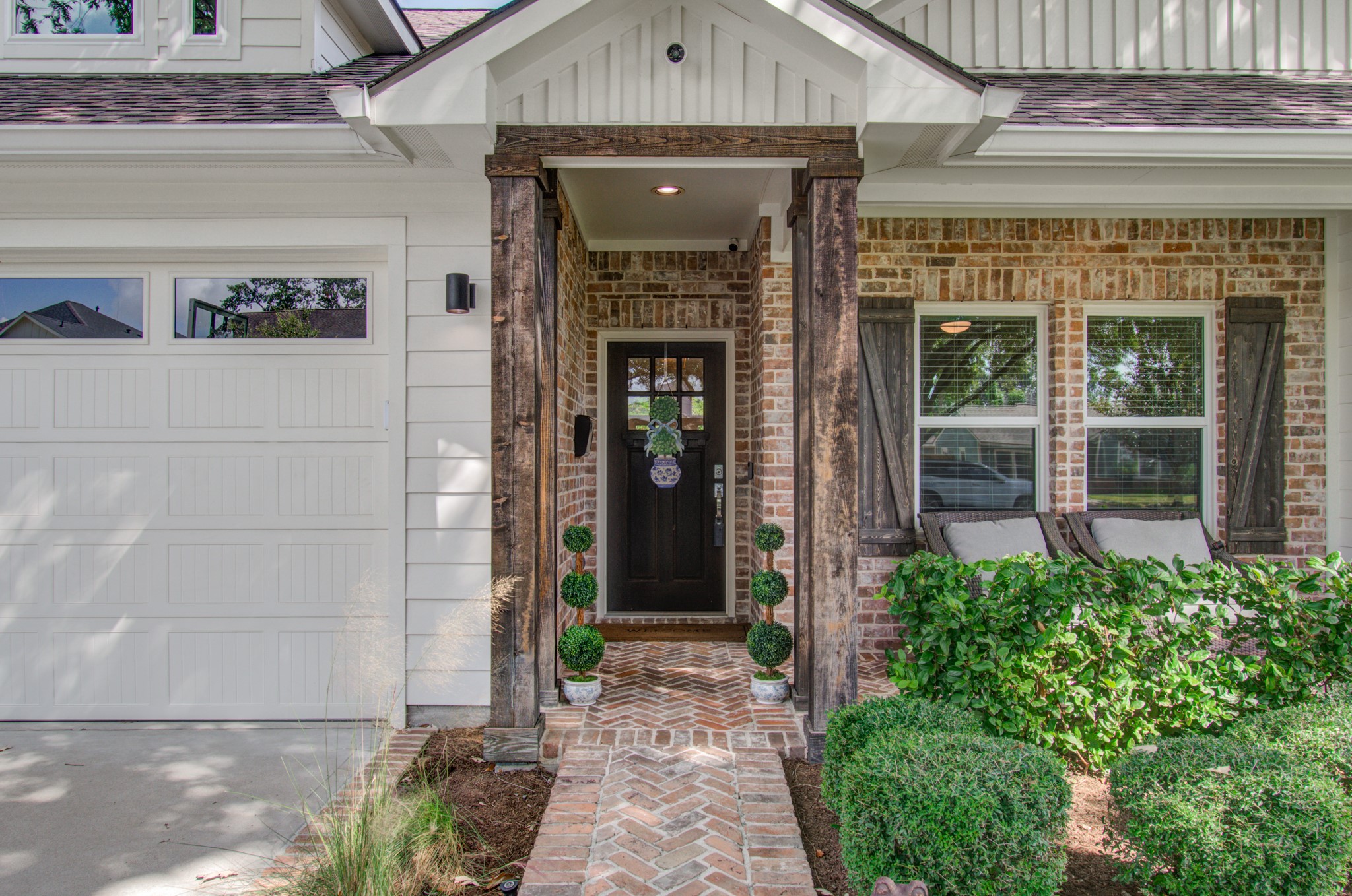 Charming entryway with rustic wooden accents, brick walkway, and lush greenery, leading to a welcoming front door.
