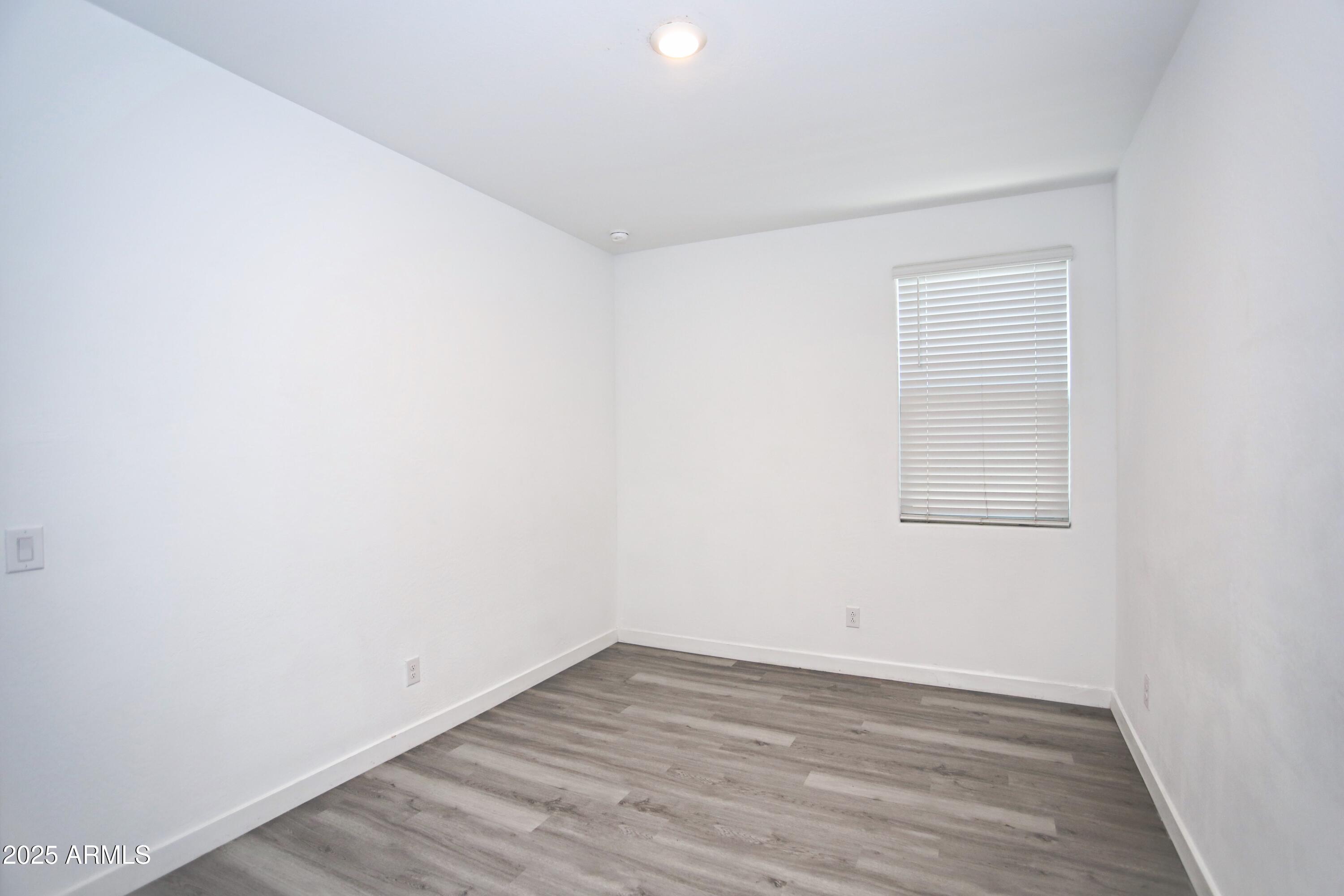 1535 West Corral Road Phoenix, AZ 85041 - Photo 14 of 39 a view of an empty room with wooden floor and a window