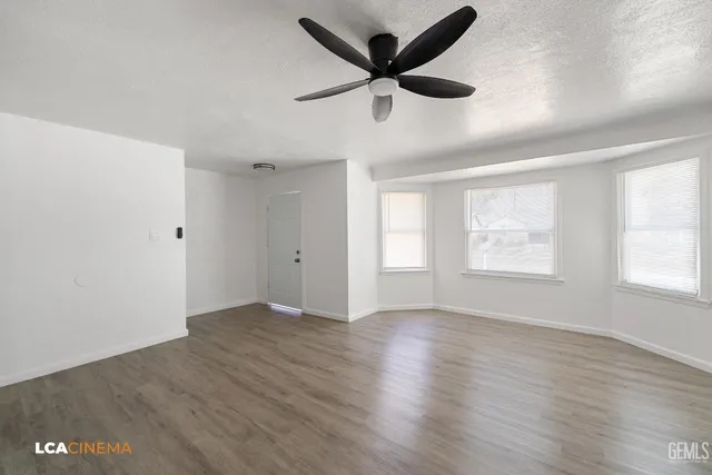 an empty room with wooden floor fan and windows