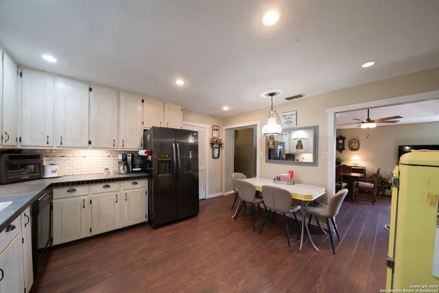 a kitchen with stainless steel appliances kitchen island granite countertop a refrigerator a stove a sink a dining table and chairs with wooden floor