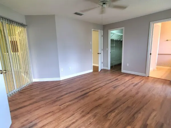 an empty room with wooden floor fan and windows