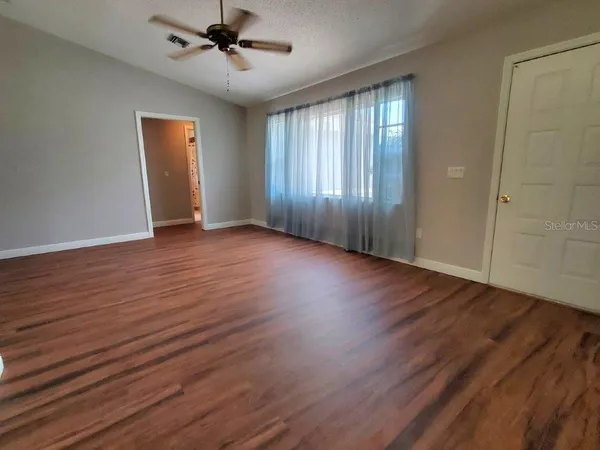 an empty room with wooden floor chandelier fan and windows