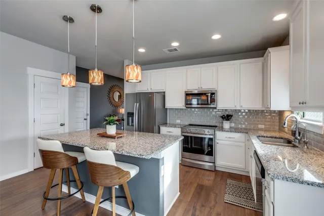 a kitchen with stainless steel appliances granite countertop a stove top oven a sink a dining table and chairs with wooden floor