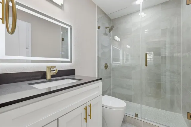 a bathroom with a granite countertop sink a toilet a mirror and shower