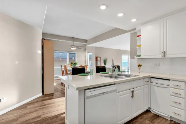 a kitchen with a sink dishwasher and white cabinets with wooden floor