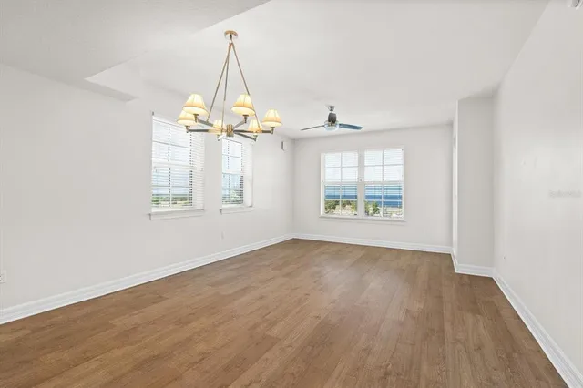 an empty room with wooden floor chandelier and windows