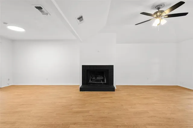 a view of an empty room with wooden floor fireplace and a window