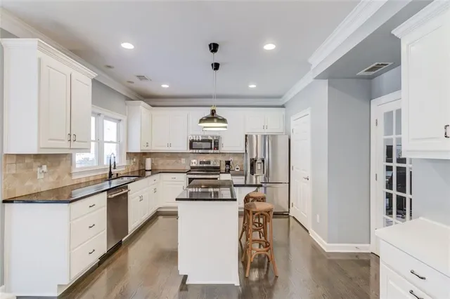 a kitchen with stainless steel appliances granite countertop a refrigerator a stove top oven a sink dishwasher and white cabinets with wooden floor