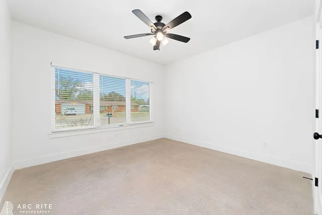 an empty room with chandelier fan and windows