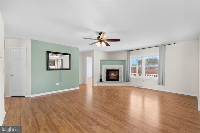 a view of an empty room with wooden floor fireplace and a window