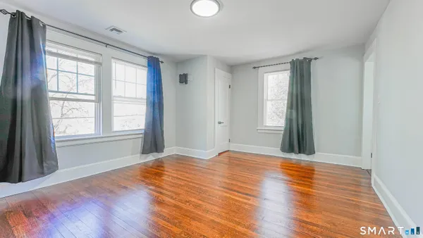a view of an empty room with wooden floor and a window