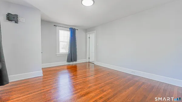 a view of an empty room with wooden floor and window