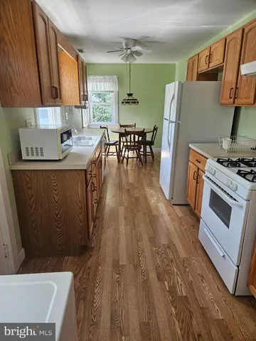 a kitchen with stainless steel appliances a stove a refrigerator a sink a dining table and chairs with wooden floor