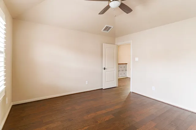 an empty room with wooden floor chandelier fan and windows