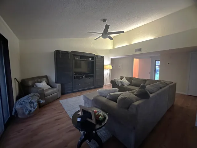 an empty room with wooden floor ceiling fan and windows