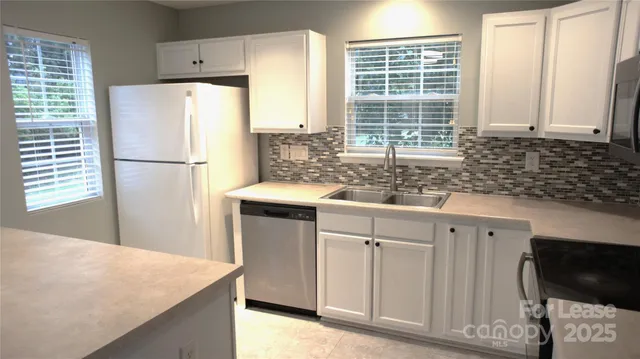 a white kitchen with sink windows and refrigerator