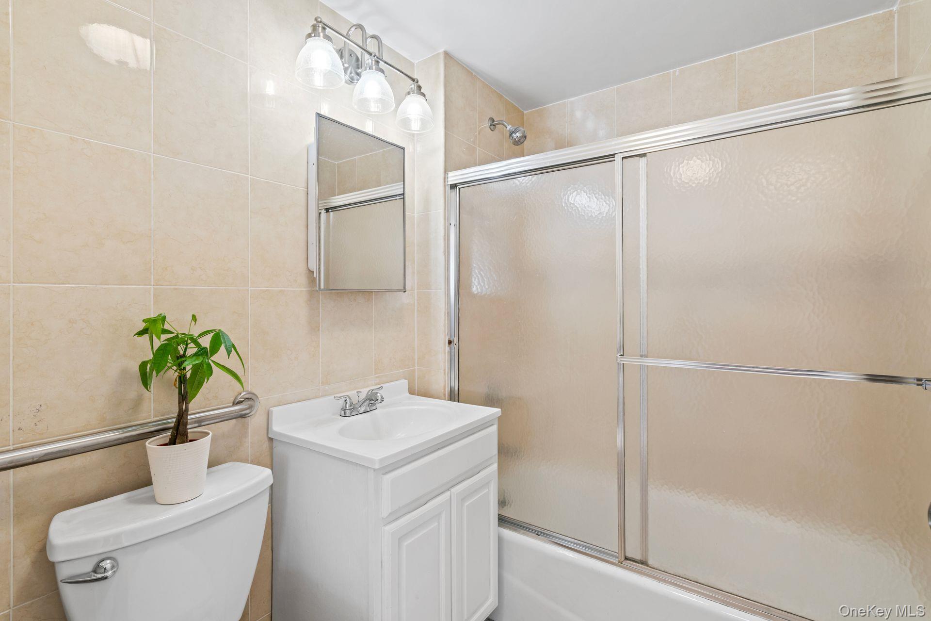 136-16 31st Road, Unit 8B Queens, NY 11354 - Photo 13 of 23 Full bathroom featuring vanity, toilet, combined bath / shower with glass door, and tile walls