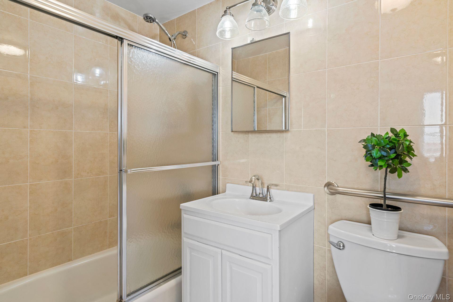 136-16 31st Road, Unit 8B Queens, NY 11354 - Photo 18 of 23 Full bathroom with toilet, vanity, shower / bath combination with glass door, and tile walls