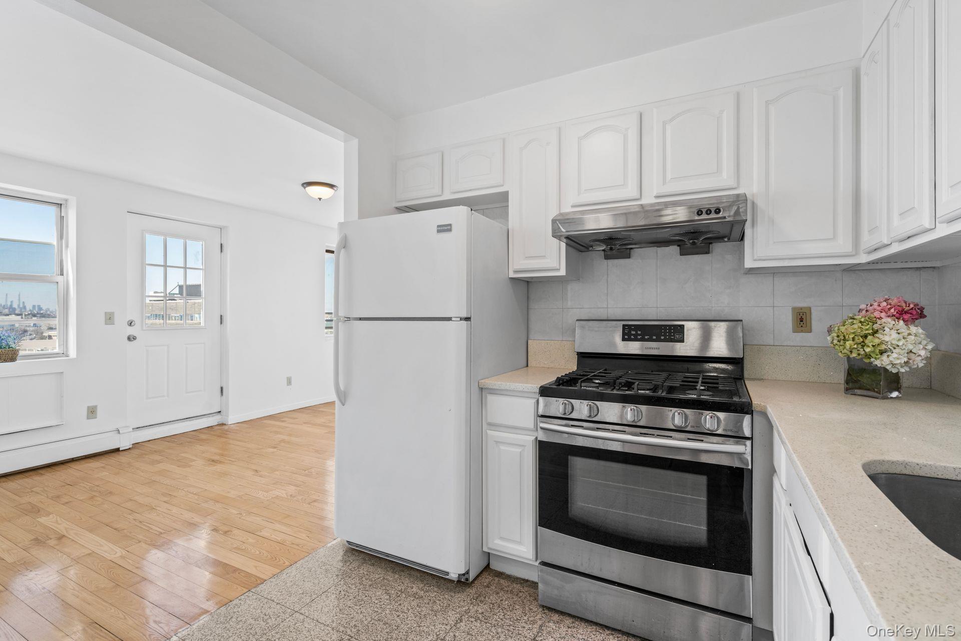 136-16 31st Road, Unit 8B Queens, NY 11354 - Photo 3 of 23 Kitchen featuring tasteful backsplash, white cabinetry, white refrigerator, gas range, and light hardwood / wood-style flooring