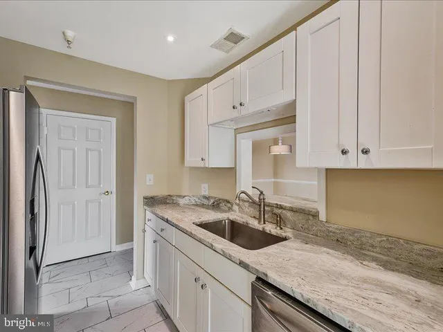 a kitchen with granite countertop a sink stainless steel appliances white cabinets and a window