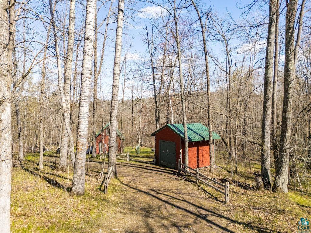 20663 Hardwood Loop Finlayson, MN 55735 - Photo 31 of 36 Wooded property with a rustic red outbuilding featuring a green roof, a second red structure in the background, a dirt path, and natural wood fencing