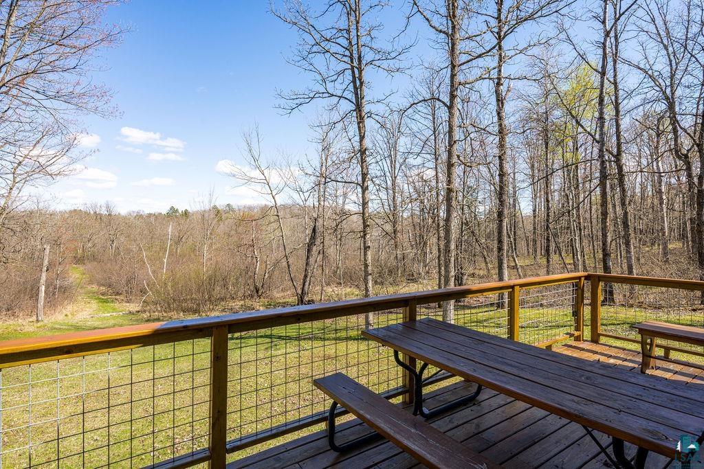 20663 Hardwood Loop Finlayson, MN 55735 - Photo 4 of 36 Expansive wooden deck with wire mesh railing overlooking a verdant landscape and mature trees