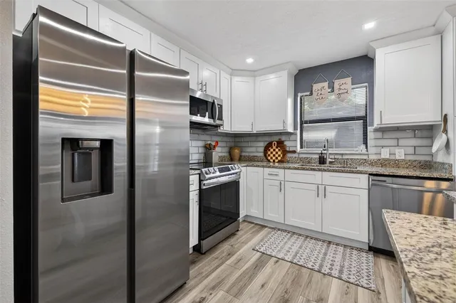 a kitchen with stainless steel appliances granite countertop a refrigerator a sink and white cabinets
