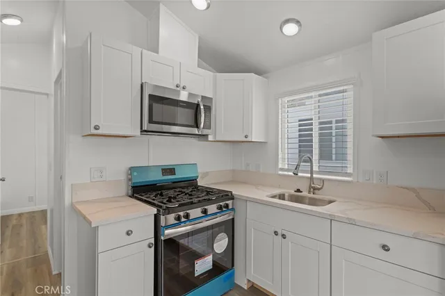 a kitchen with stainless steel appliances granite countertop white cabinets a sink a stove a window and white cabinets
