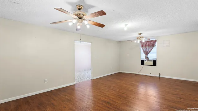 an empty room with wooden floor chandelier fan and windows
