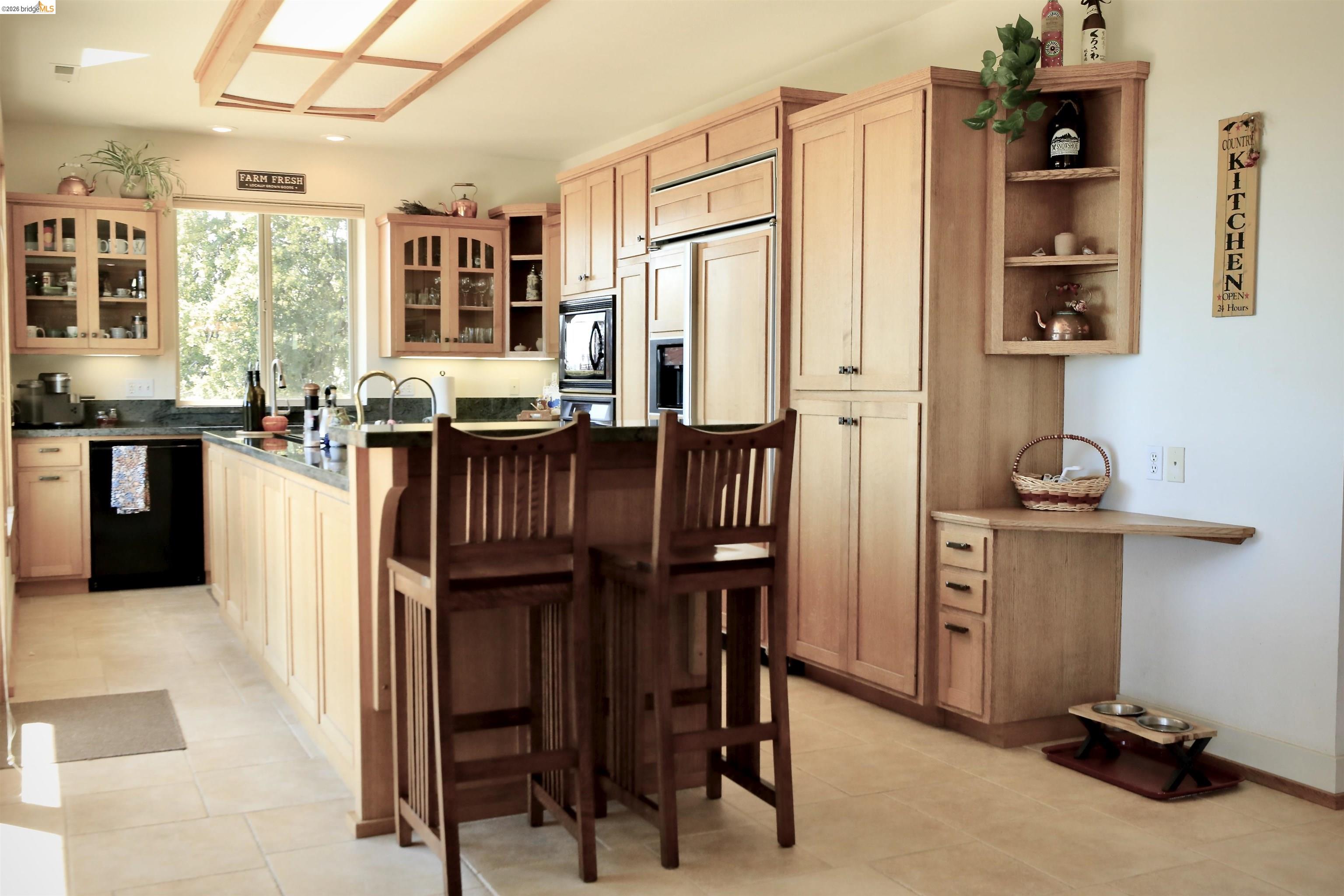 18288 Lambert Lake Road Sonora, CA 95370 - Photo 10 of 55 Kitchen featuring a kitchen island with sink, a kitchen bar, black appliances, glass fronted cabinets, and light wood finish cabinetry
