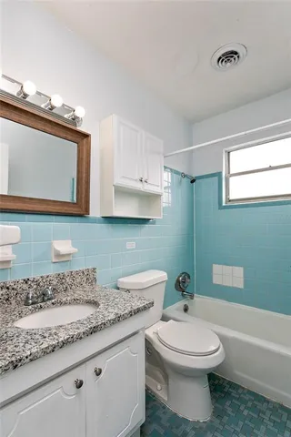 a bathroom with a granite countertop toilet a mirror and bathtub