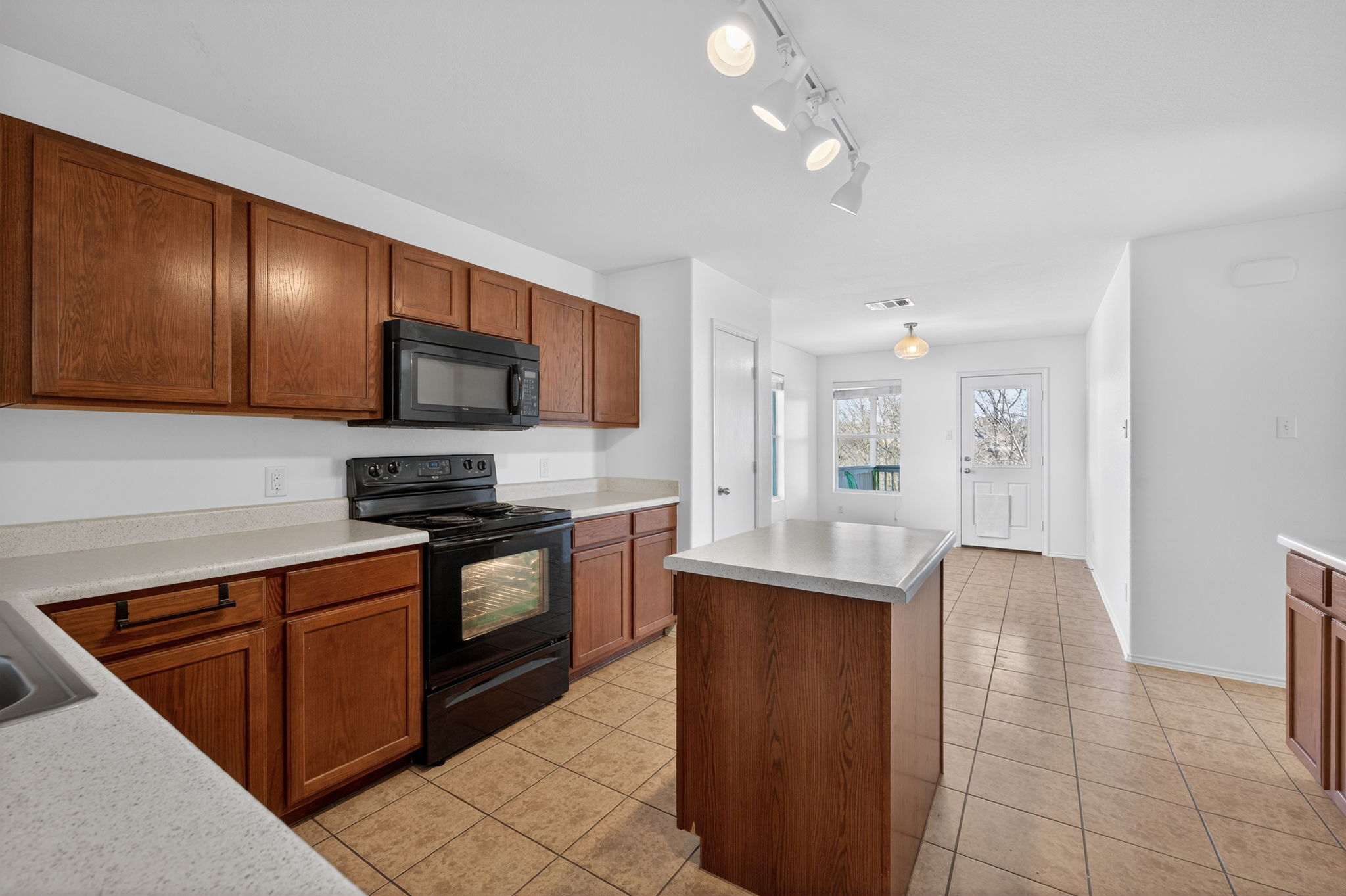 13629 Coomer Path Pflugerville, TX 78660 - Photo 8 of 30 Kitchen with black appliances, wood finish cabinets, light tile patterned floors, a kitchen island, and track lighting