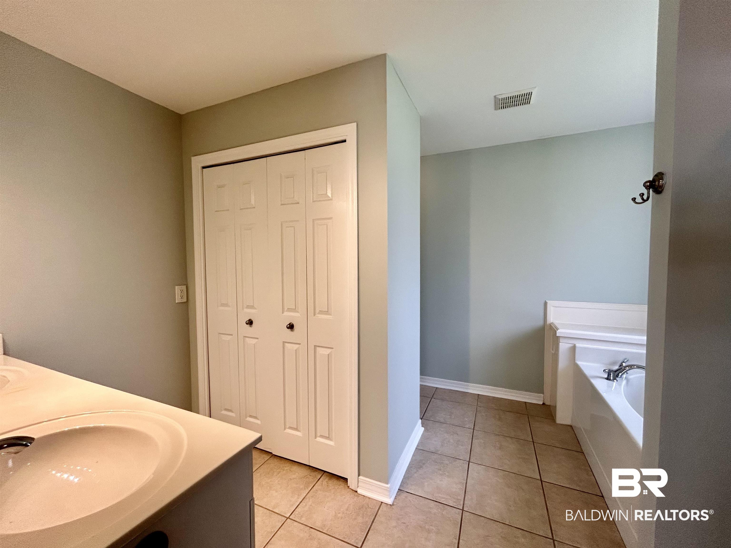 7198 Raintree Lane Gulf Shores, AL 36542 - Photo 15 of 33 Double vanity with integrated sinks, bi-fold closet doors, built-in bathtub, and ceramic tile flooring