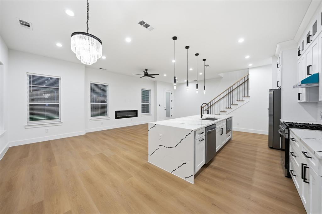 306 East 7th Street Dallas, TX 75203 - Photo 7 of 22 Open concept living space featuring wood-finish flooring, a contemporary kitchen island with a waterfall countertop, white cabinetry with matte black hardware, a built-in electric fireplace, and a modern chandelier