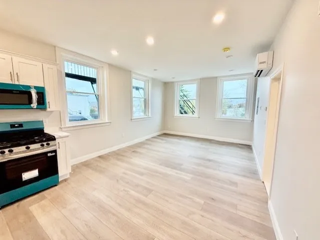 a view of a kitchen and an empty room with wooden floor and windows