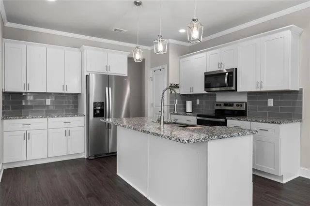 a kitchen with kitchen island granite countertop stainless steel appliances a sink stove a refrigerator a center island with wooden floor and cabinets