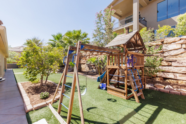 1257 West 2320 South St. George, UT 84770 - Photo 35 of 55 Backyard featuring artificial turf, a wood playset, and terraced landscaping with mature trees and rock retaining walls
