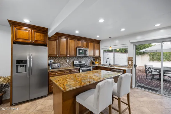 a kitchen with stainless steel appliances granite countertop a refrigerator a stove a sink a dining table and chairs with wooden floor