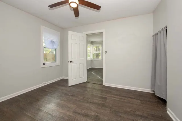 an empty room with wooden floor chandelier fan and windows