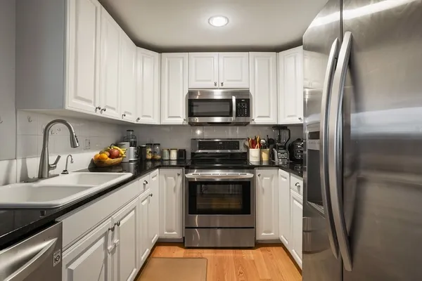 a kitchen with granite countertop a refrigerator sink and white cabinets