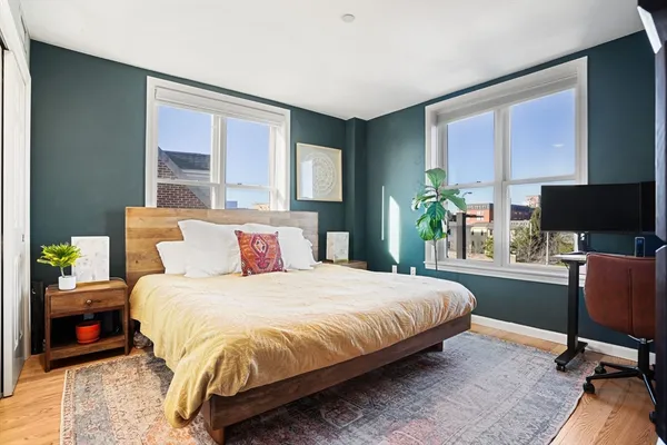 a bedroom with a bed a large window and potted plant on the dresser